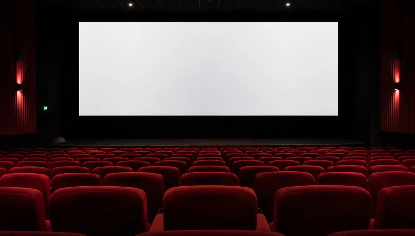 Rows of empty cinema seats facing a large blank screen, lit by dim ambient lighting