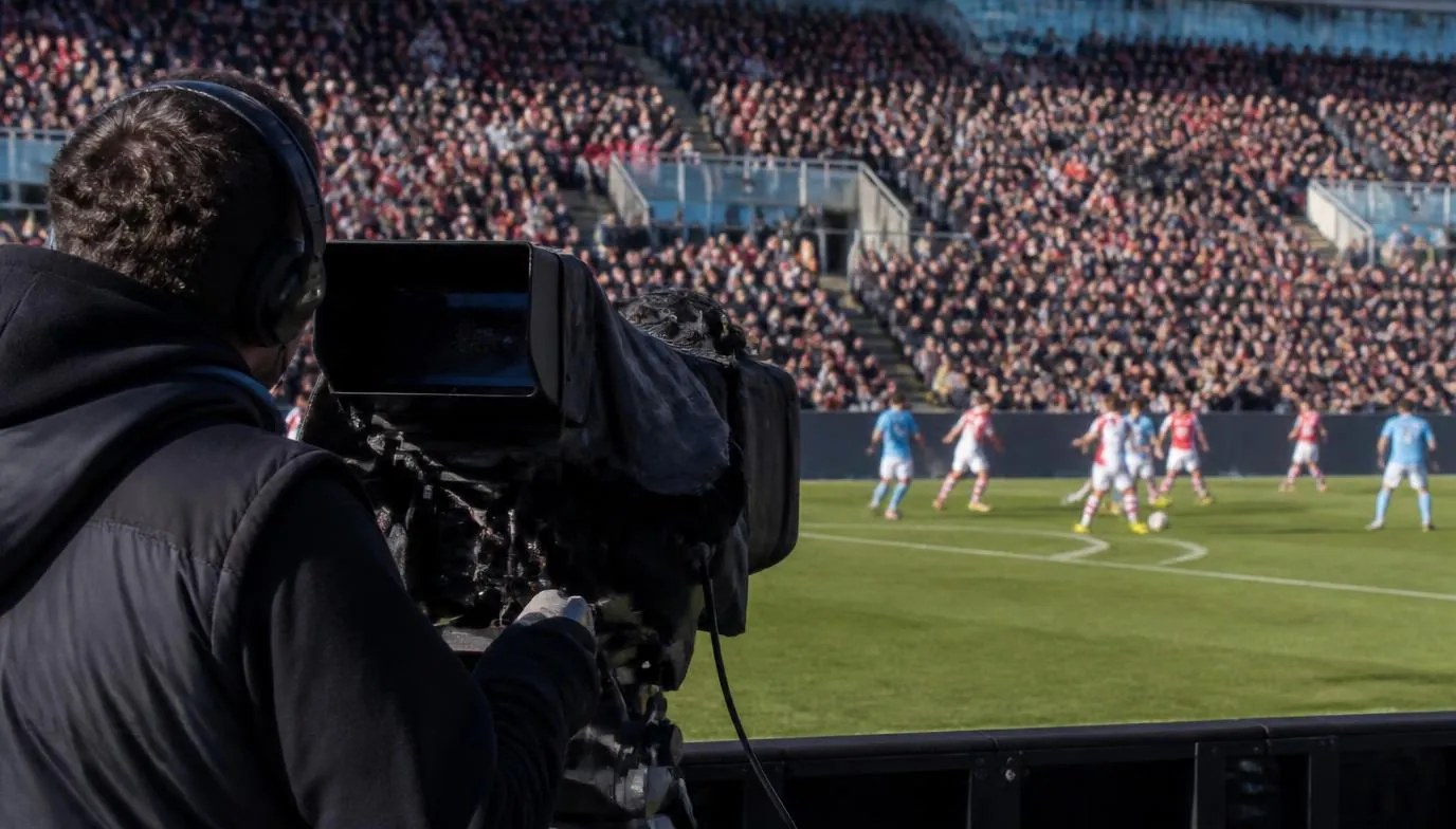 Television production crew filming a packed stand at a women's football fixture